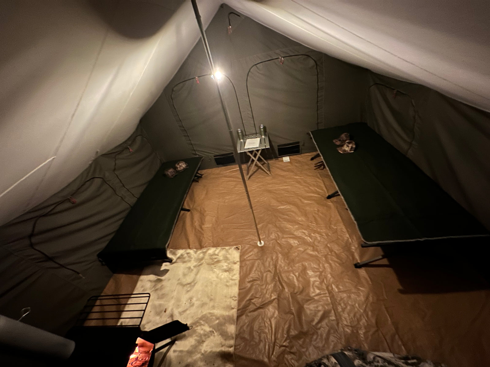 Inside a canvas wall tent with cots and a lantern