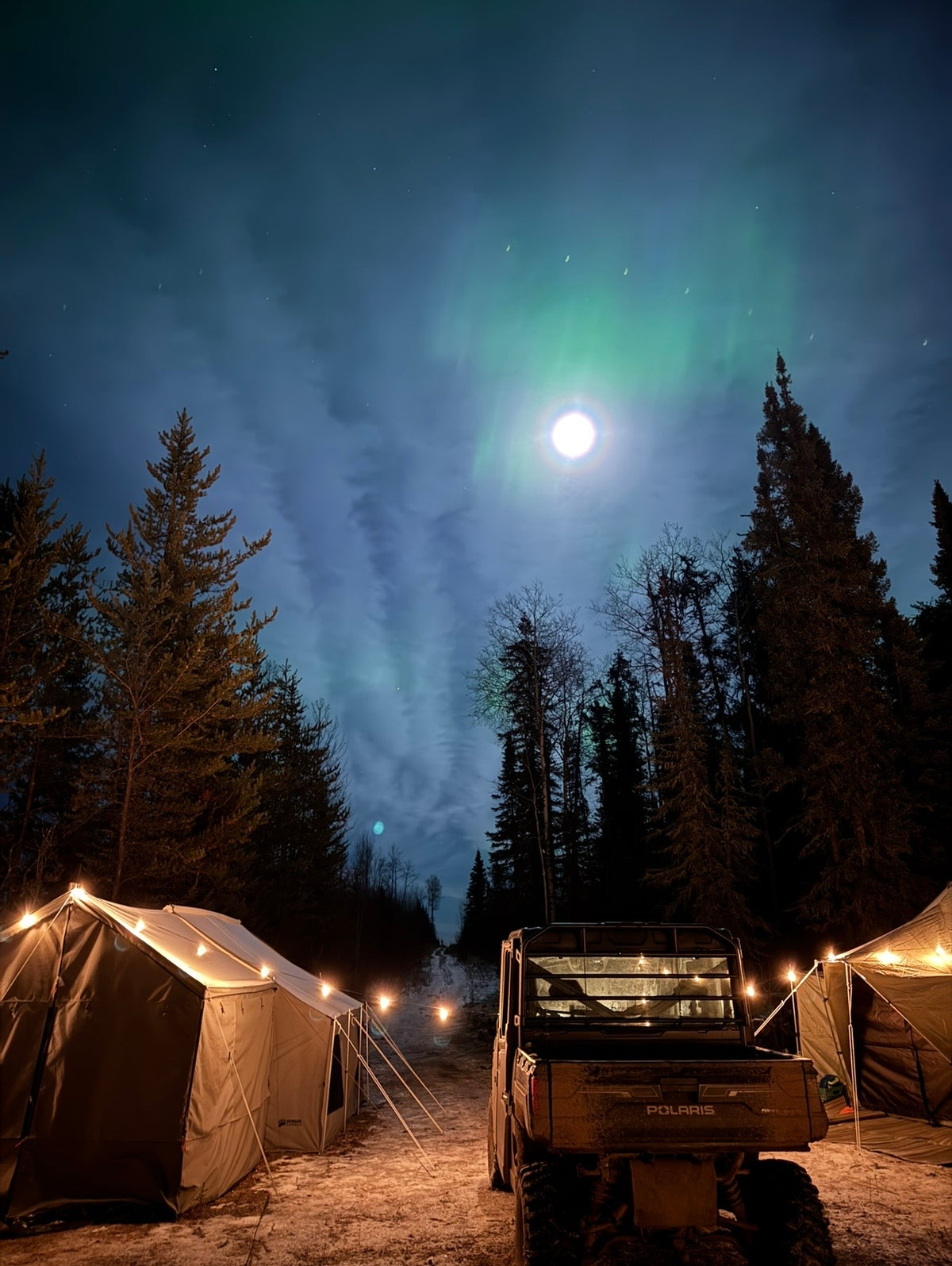 Canvas wall tents lit from inside under the northern lights