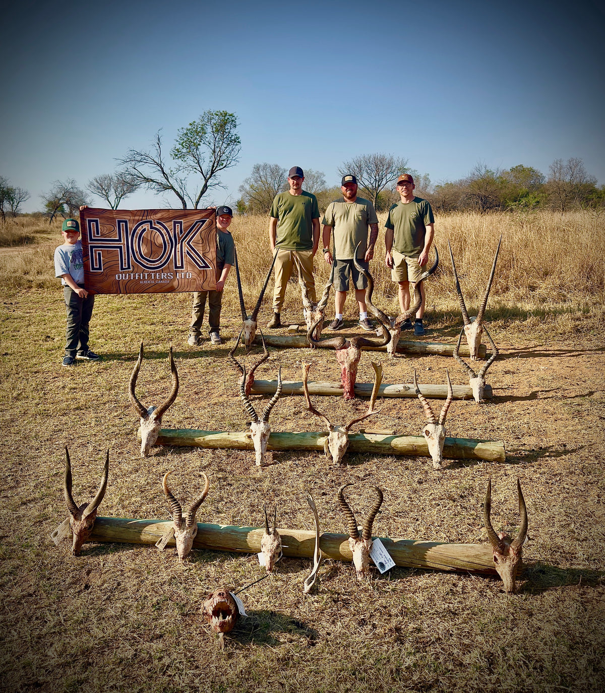 The HOK Africa group with the HOK Outfitters flag and a season of plains game trophies laid out on logs